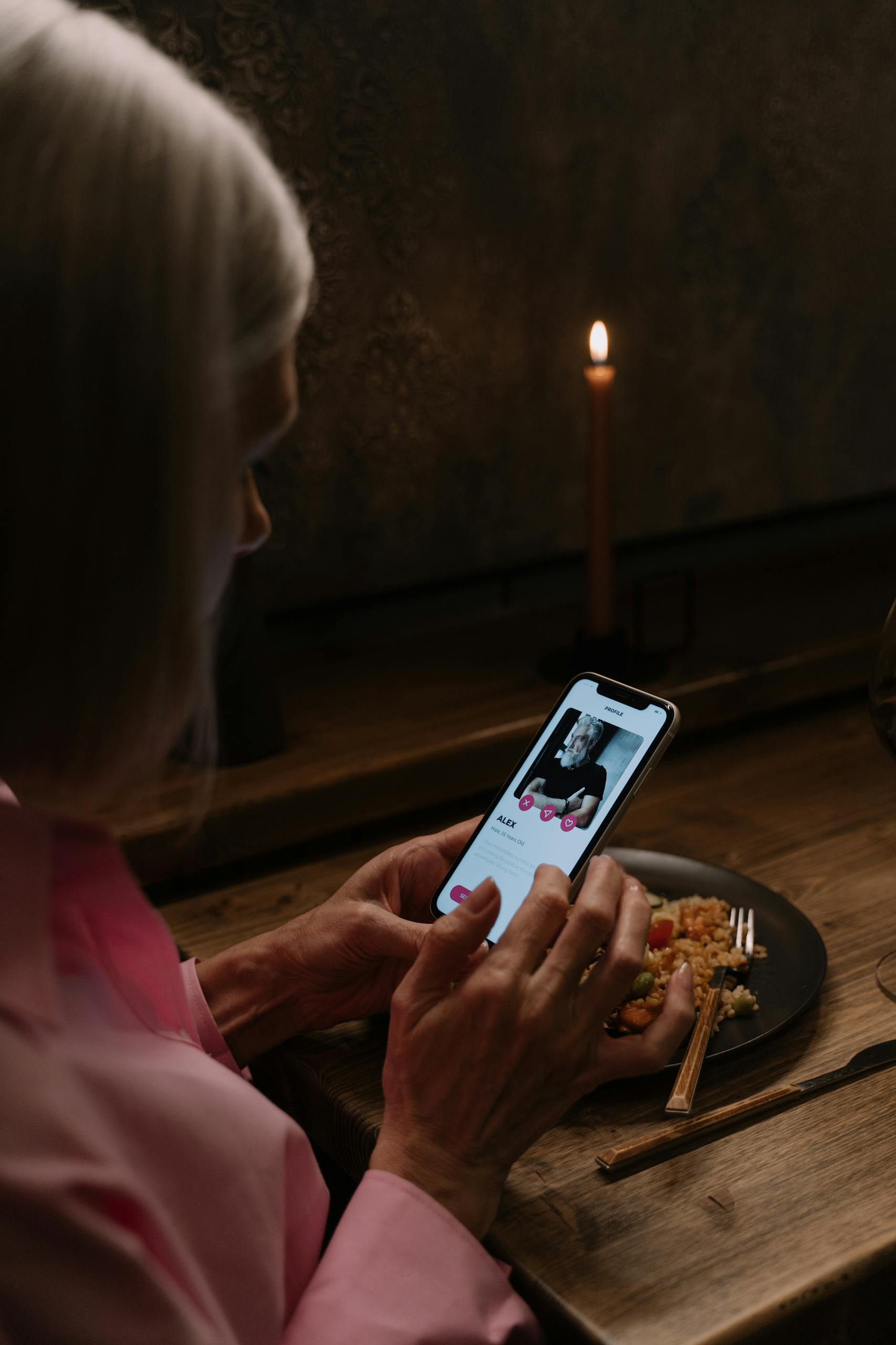 Elderly woman using dating app on smartphone, dining table.