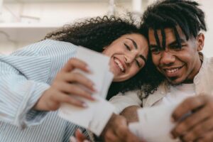 Smiling interracial couple enjoying memories together, looking at photos indoors. Warm and candid moment.