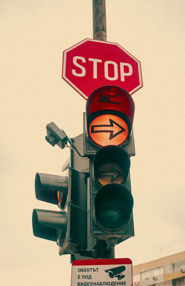 A vintage-style traffic light with a stop sign and yellow arrow, urban setting.