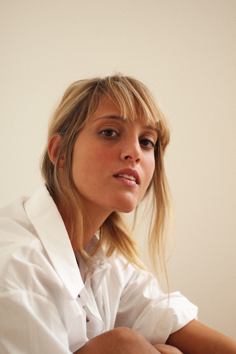 A young woman poses casually in a white shirt.