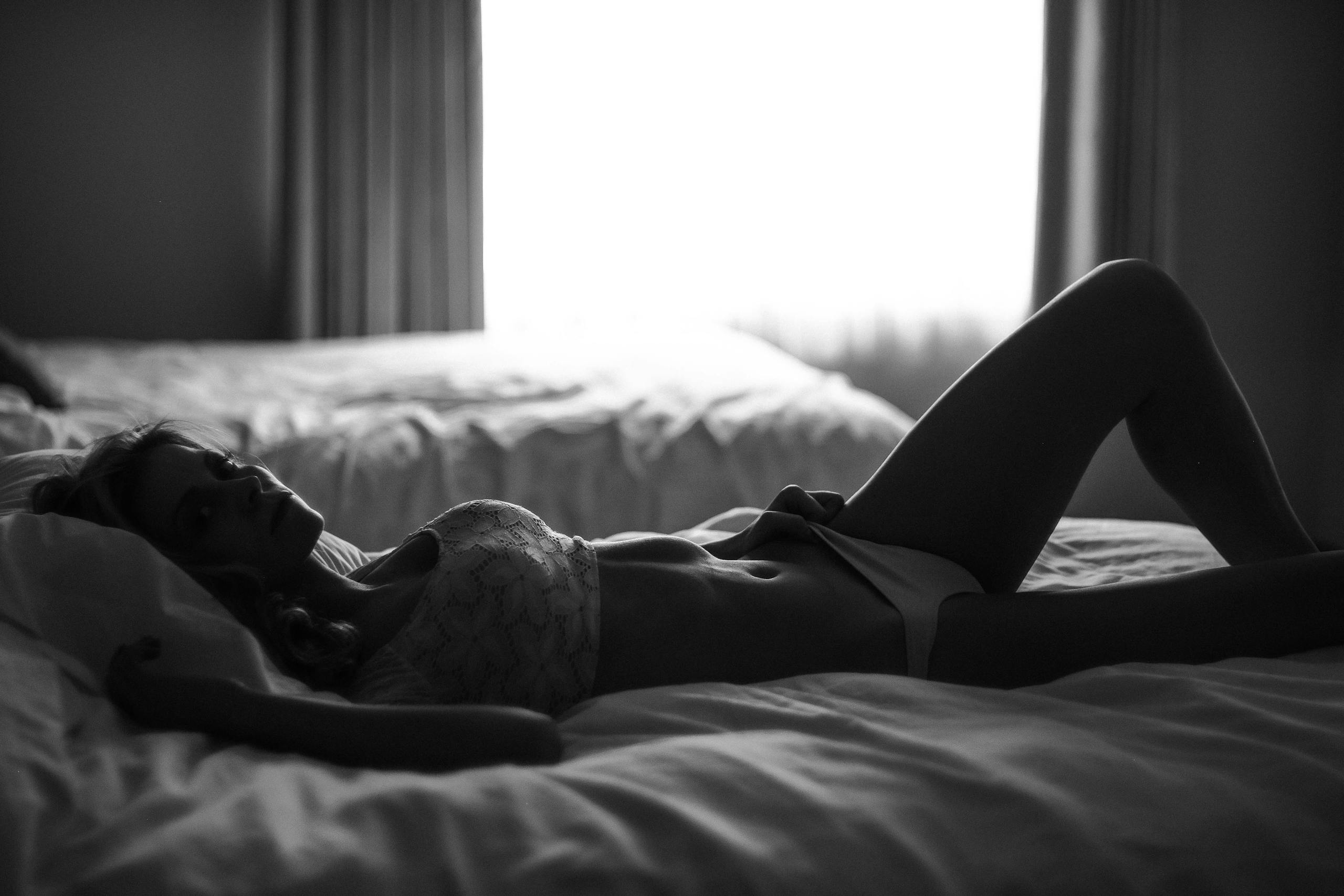 Artistic silhouette of a woman in lingerie reclining on a bed in muted lighting.