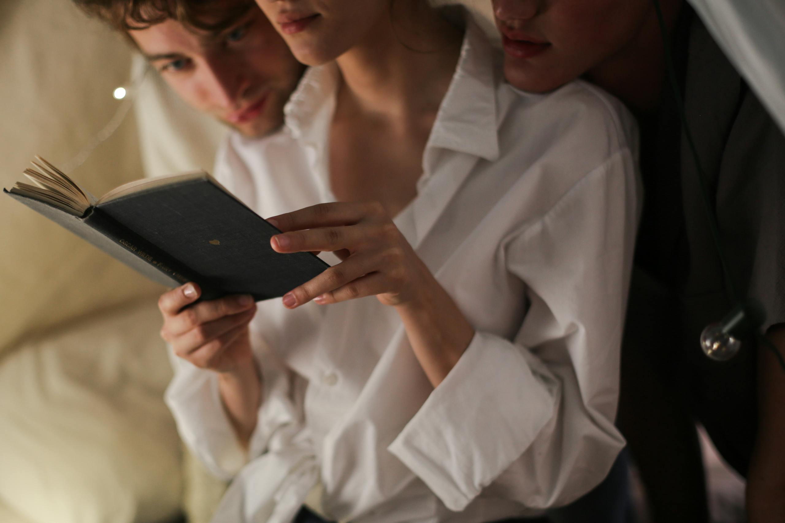 Close-up of three people reading together in a cozy indoor setting, highlighting intimacy and connection.
