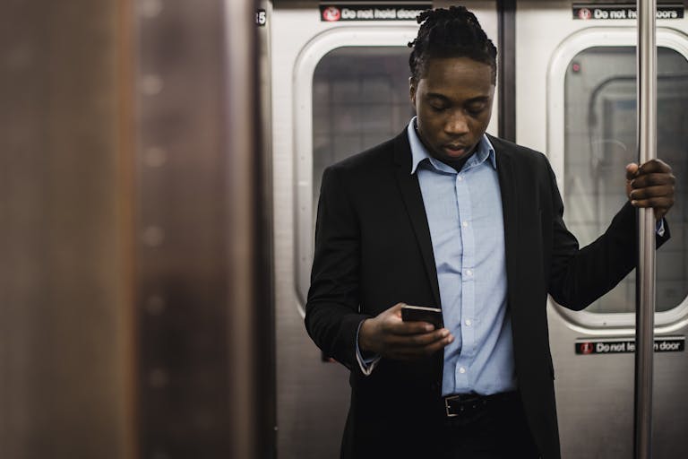 African American office worker surfing net on mobile phone while getting home by subway
