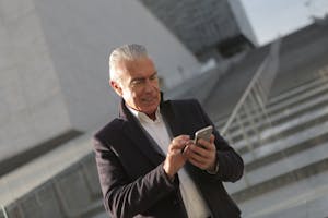 Elderly man in business attire using smartphone outside modern building.